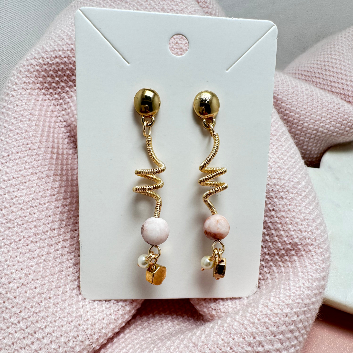 Gold-tone pierced stud earrings featuring a wrapped wire spiral design, accented with a lustrous pearl and sleek gold-tone hexagon charm. A lightweight, versatile blend of classic sophistication and modern elegance.