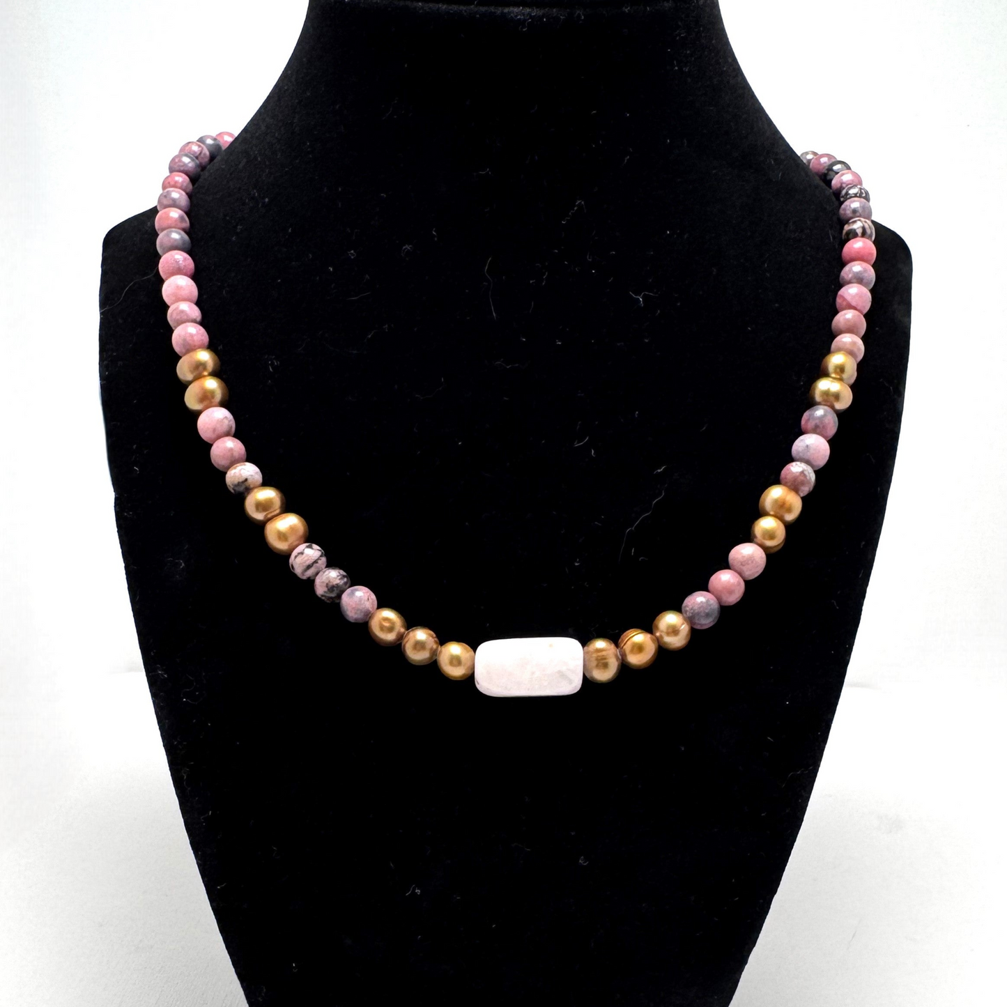 Handmade 19-inch necklace featuring rhodonite, gold-colored pearls, and a rose quartz centerpiece, symbolizing love and serenity. Finished with a gold-tone hand-forged wire hook clasp for a unique artisan touch.