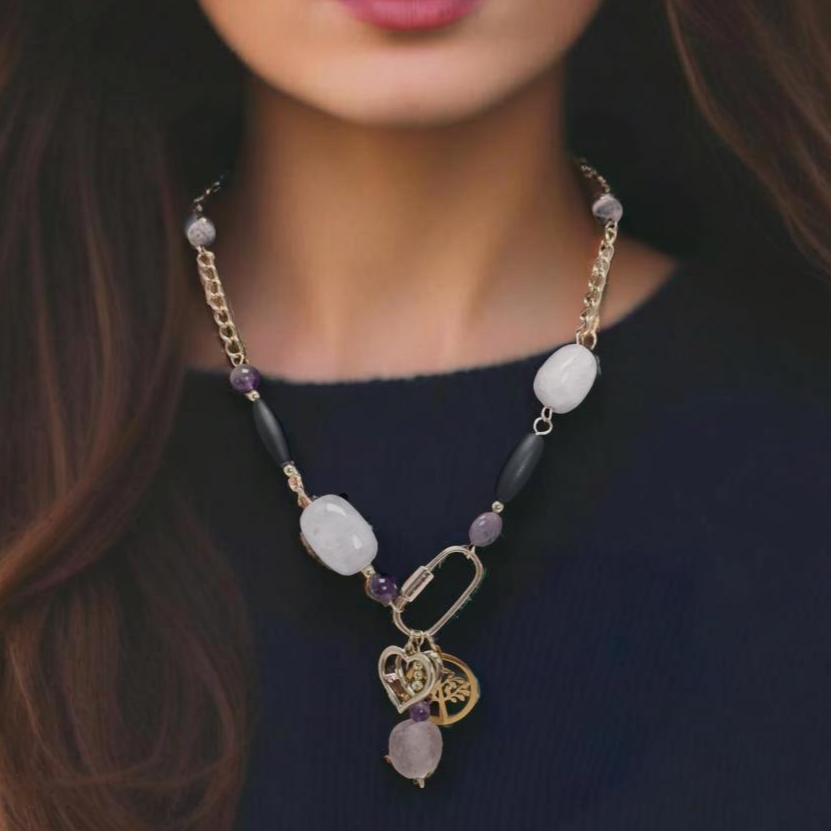 A handcrafted necklace with rose quartz, amethyst, and agate beads, featuring a carabiner with three symbolic charms: a Tree of Life, a heart, and pink sea glass with a gold heart.
