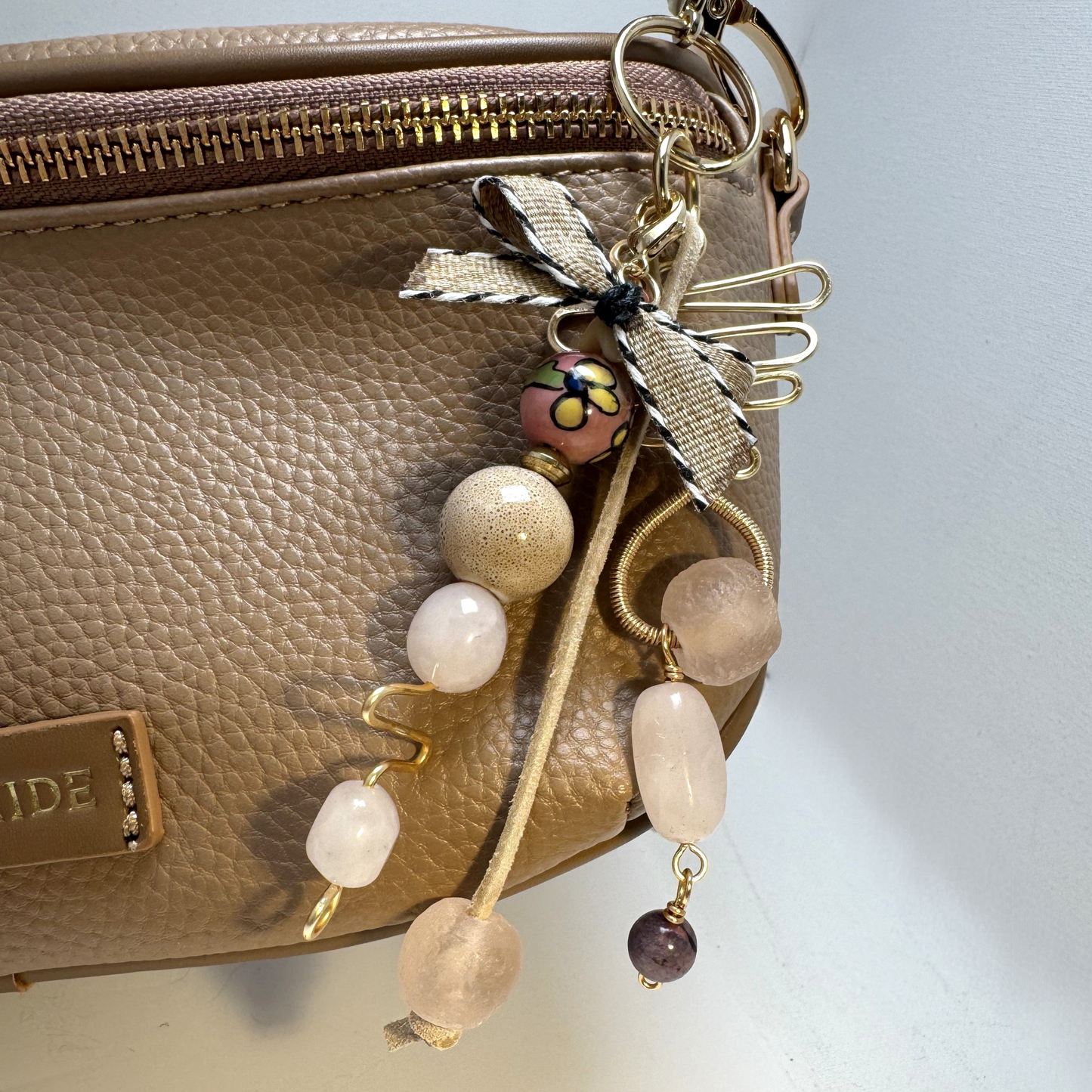 Handmade purse charm with rose quartz, sea glass, ceramic beads, gold-tone wire, and a detachable bow. Clips to bags, belts, and jean loops.