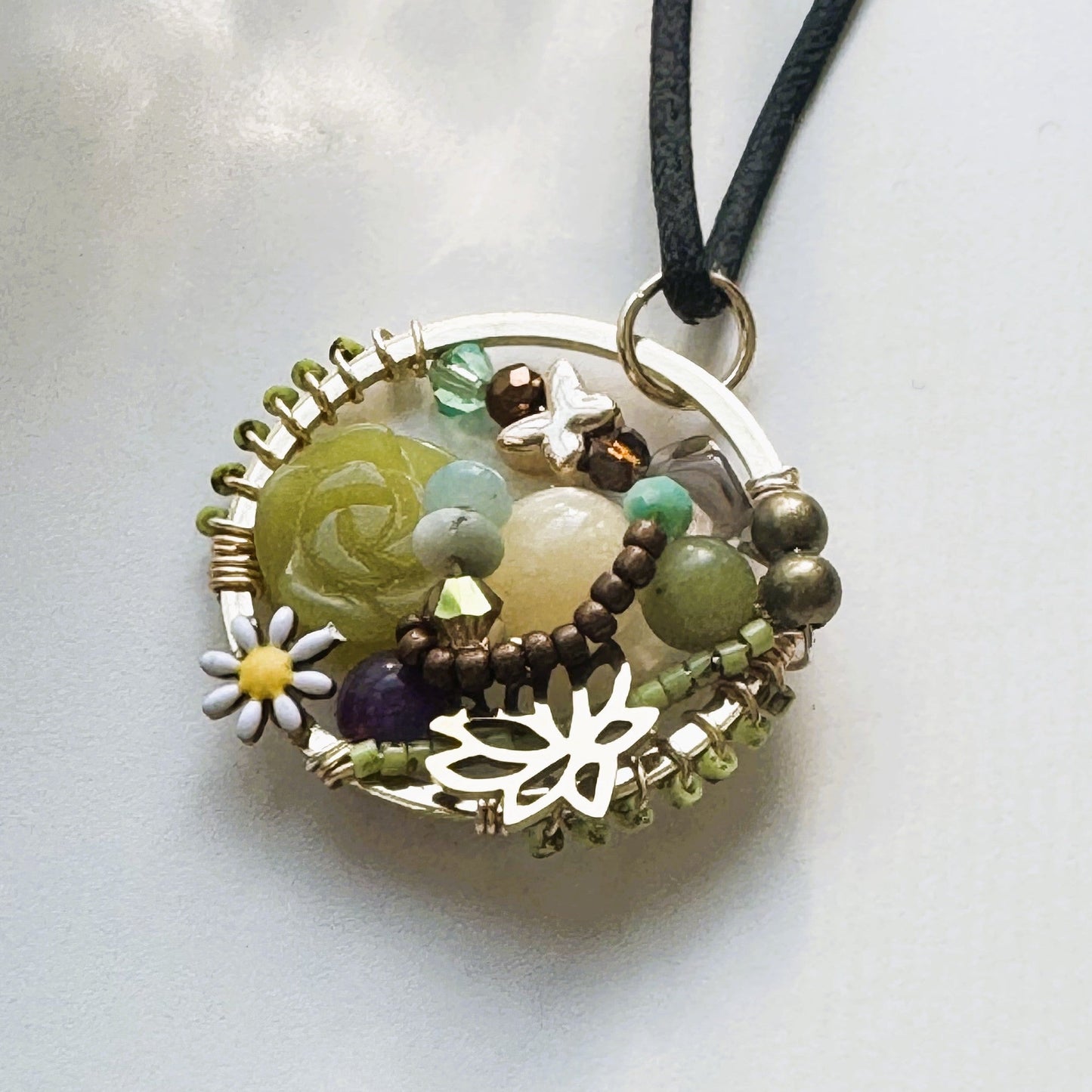 Handmade Halo pendant featuring semi-precious stones, daisy detail, butterfly accent, and mixed beads on a black cord necklace.