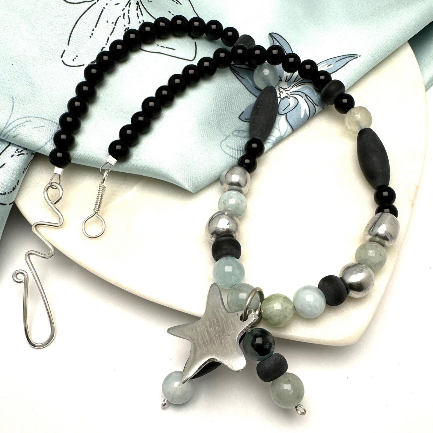 A handcrafted 18-inch necklace featuring a mix of black jasper, aquamarine, and aluminum beads, accented with a charming star pendant. Finished with a signature handmade hook clasp, this unique piece blends natural stones with modern materials for a versatile, stylish look. Handmade with care by Lacey & Bohème in Canada.