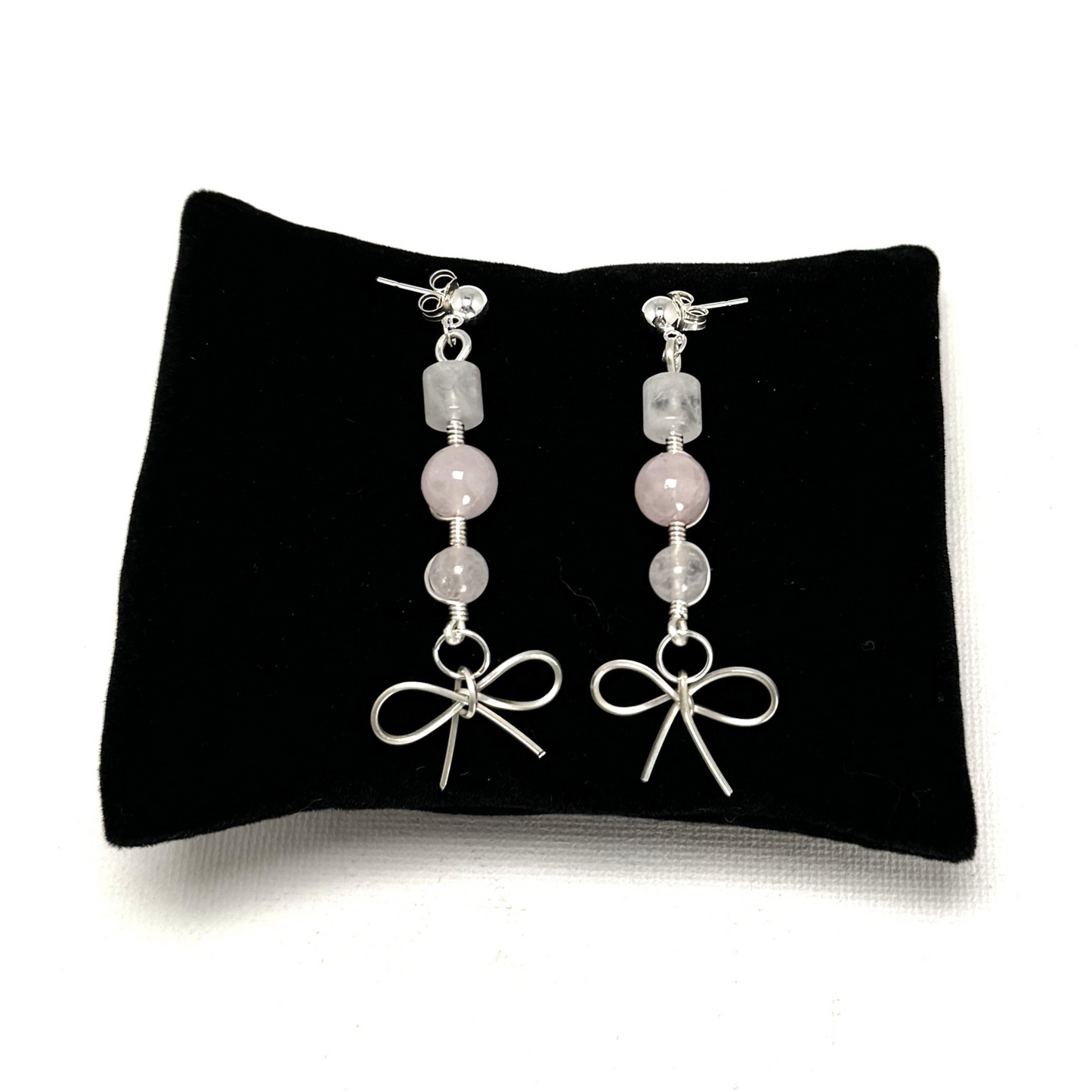 A pair of handcrafted rose quartz drop earrings featuring a delicate sterling silver bow accent and sterling silver ear posts. Elegant and feminine, measuring 2 inches (5 cm).