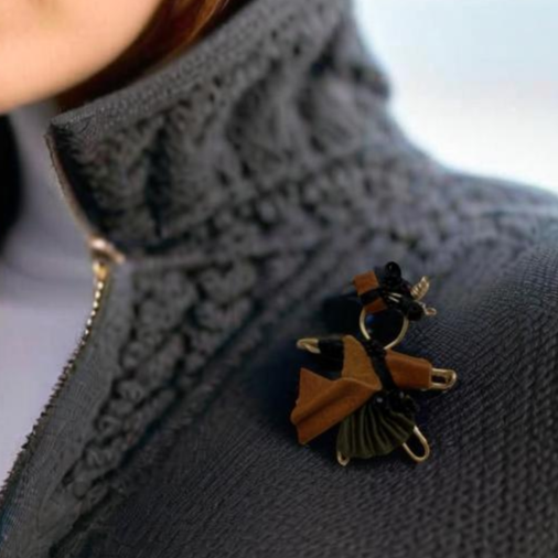 The Pixie Pin is a handcrafted brooch made from rich brown suede, recycled silk, beads, and wire, embodying strength, resilience, and the adventurous spirit of the pixie realm. Perfect for jackets, scarves, or bags