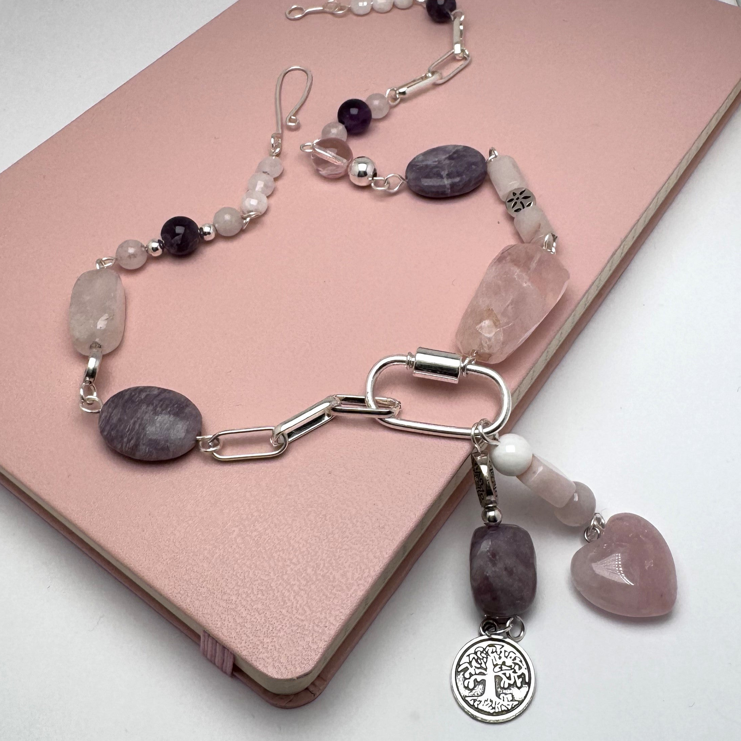 Bold 18-inch silver necklace featuring rose quartz, amethyst, and pink opal stones in an asymmetrical design. Dangled charms include a rose quartz heart with pink opal and an amethyst paired with a Tree of Life charm. A timeless, modern accessory perfect for day-to-night wear.