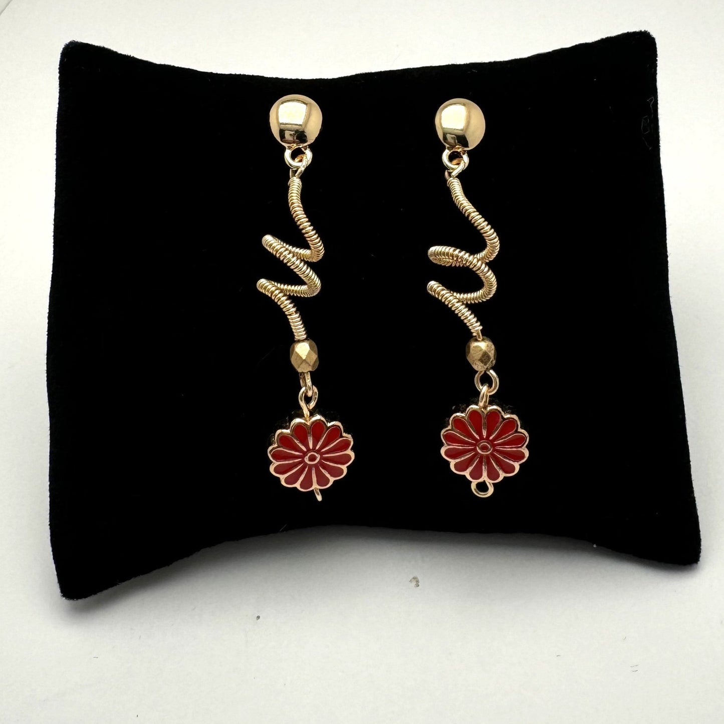 A pair of handcrafted spiral dangle earrings featuring a bold red metal flower accent. These unique earrings add a vibrant and artistic touch to any outfit. Handmade with care by Lacey & Bohème in Canada.