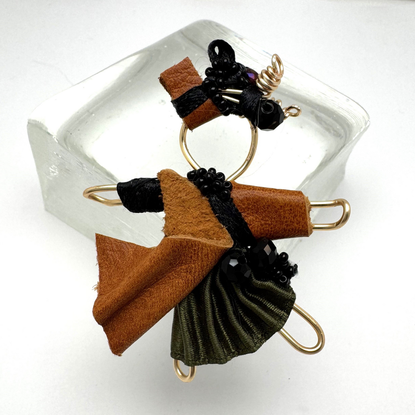 The Pixie Pin is a handcrafted brooch made from rich brown suede, recycled silk, beads, and wire, embodying strength, resilience, and the adventurous spirit of the pixie realm. Perfect for jackets, scarves, or bags.