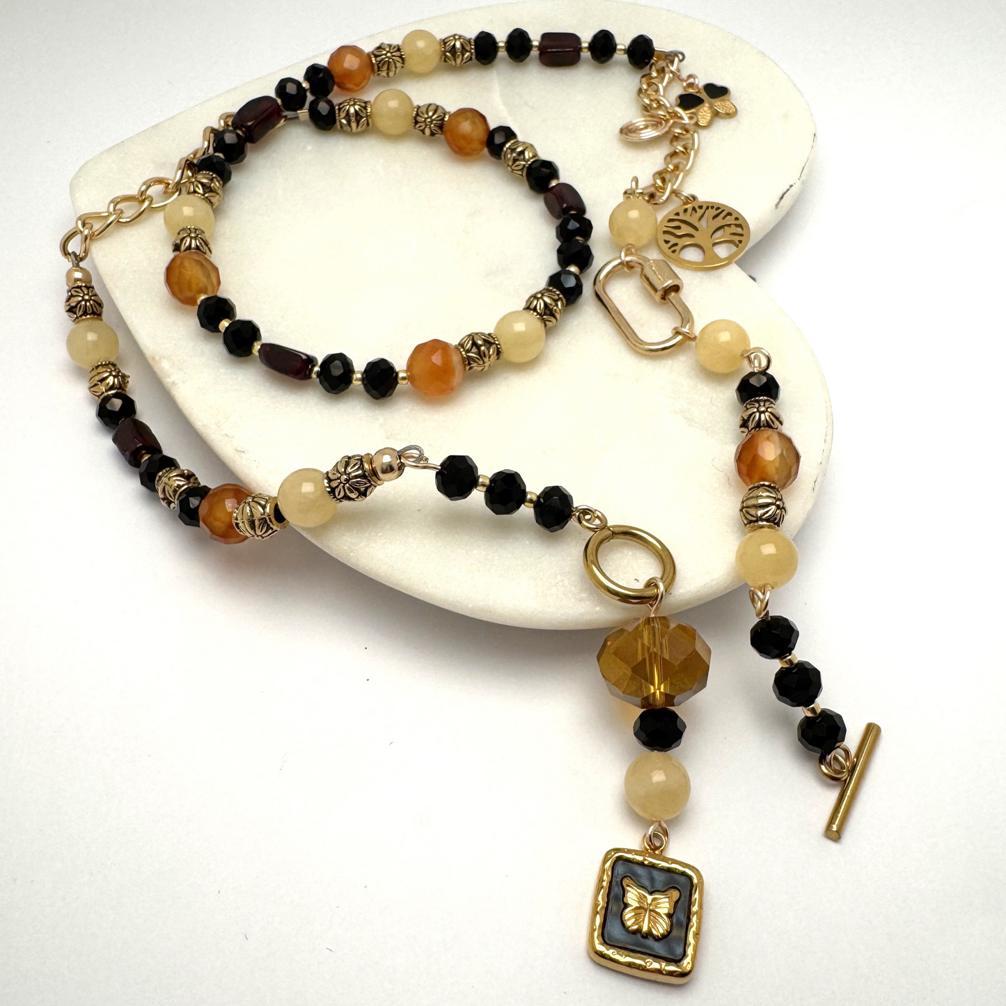 A handcrafted 24-inch necklace featuring a radiant mix of citrine, agate, and garnet beads, symbolizing warmth, grounding, and passion. Designed with a modern front toggle clasp, a bold carabiner accent, and a symbolic Tree of Life charm, this piece blends earthy elegance with contemporary style. Perfect for layering or wearing solo, this Lacey & Bohème creation celebrates growth and personal empowerment. Made in Canada.