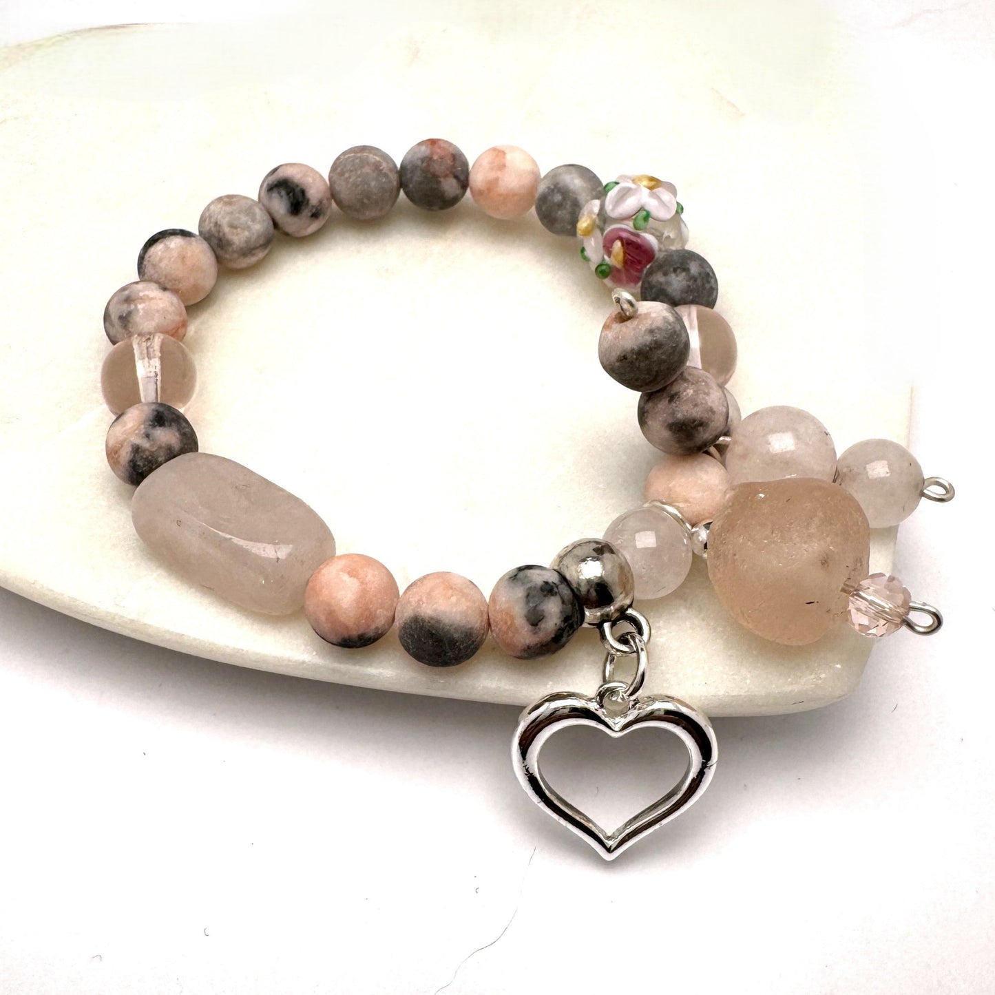 Feminine Rose Garden Stretch Bracelet with rose quartz and rhodonite beads, featuring a lampwork floral glass bead, silver-plated heart, and sea glass charm. A romantic and meaningful accessory, finished with a handmade bead tie for a unique, artisanal touch. Perfect for Valentine's Day or as a personal keepsake.