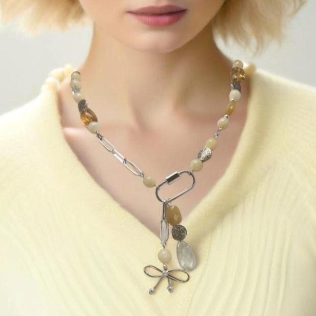A modern asymmetric necklace featuring a sleek silver chain, vibrant citrine beads, and a silver carabiner clasp holding two unique pendants—a playful bow charm and a mix of citrine beads with a textured silver accent. Finished with a handmade hook clasp, this bold statement piece combines style with citrine’s uplifting energy.