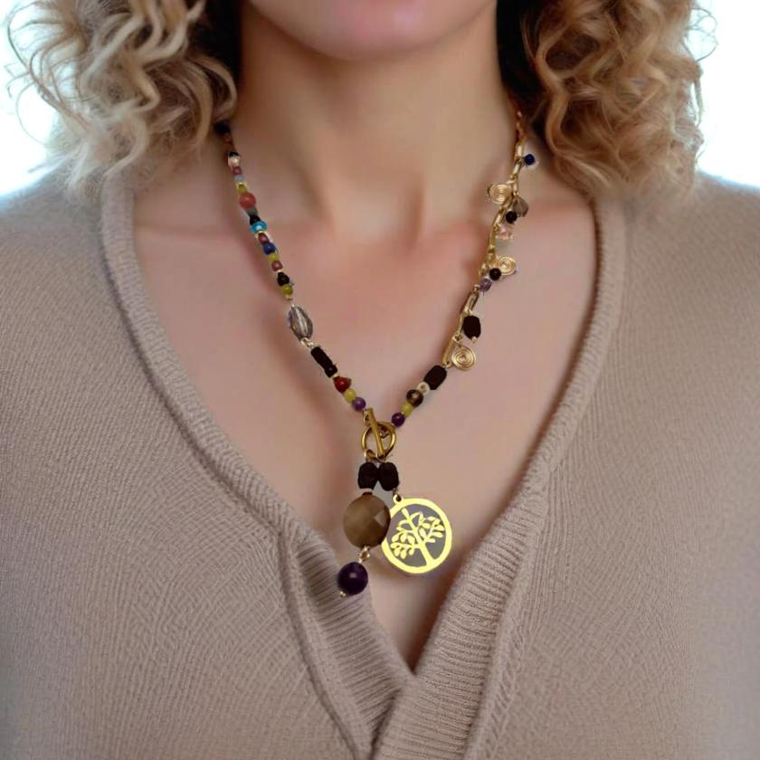A handcrafted necklace featuring semi-precious stones, ceramic accents, and glass beads, with a modern paperclip chain and delicate stone charms. Anchored by a handmade charm with a trio of beads and a symbolic Tree of Life pendant, this 23-inch necklace by Lacey & Bohème embodies connection, growth, and artisanal beauty. Perfect for everyday wear or special occasions.