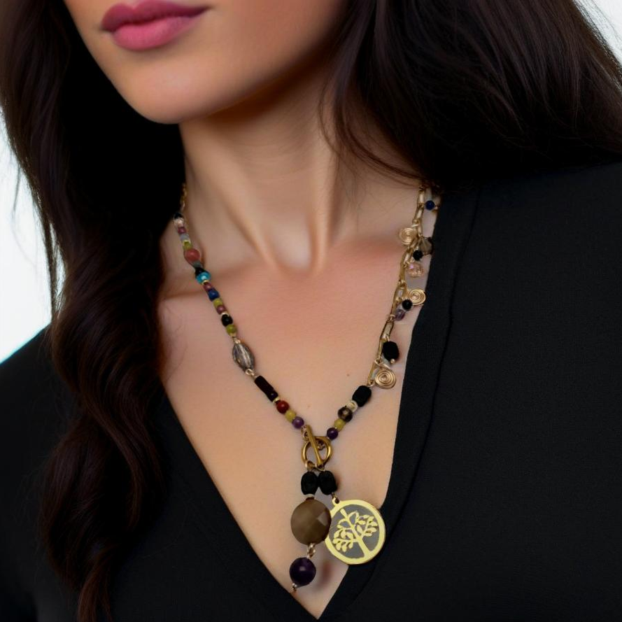 A handcrafted necklace featuring semi-precious stones, ceramic accents, and glass beads, with a modern paperclip chain and delicate stone charms. Anchored by a handmade charm with a trio of beads and a symbolic Tree of Life pendant, this 23-inch necklace by Lacey & Bohème embodies connection, growth, and artisanal beauty. Perfect for everyday wear or special occasions.