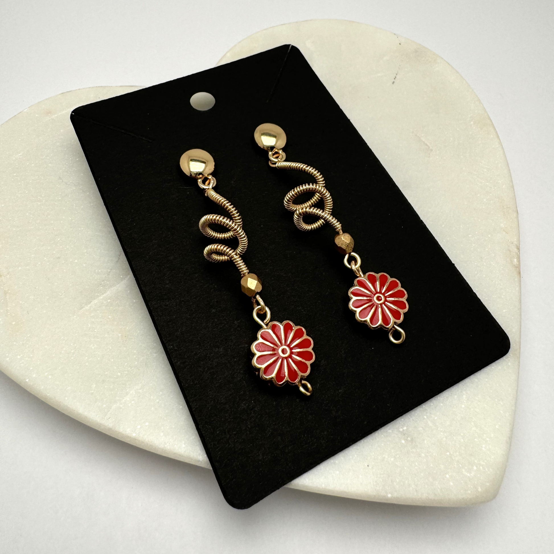 A pair of handcrafted spiral dangle earrings featuring a bold red metal flower accent. These unique earrings add a vibrant and artistic touch to any outfit. Handmade with care by Lacey & Bohème in Canada.