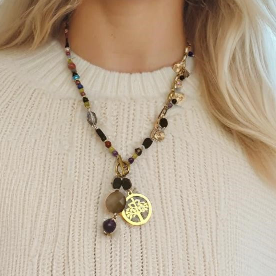 A handcrafted necklace featuring semi-precious stones, ceramic accents, and glass beads, with a modern paperclip chain and delicate stone charms. Anchored by a handmade charm with a trio of beads and a symbolic Tree of Life pendant, this 23-inch necklace by Lacey & Bohème embodies connection, growth, and artisanal beauty. Perfect for everyday wear or special occasions.
