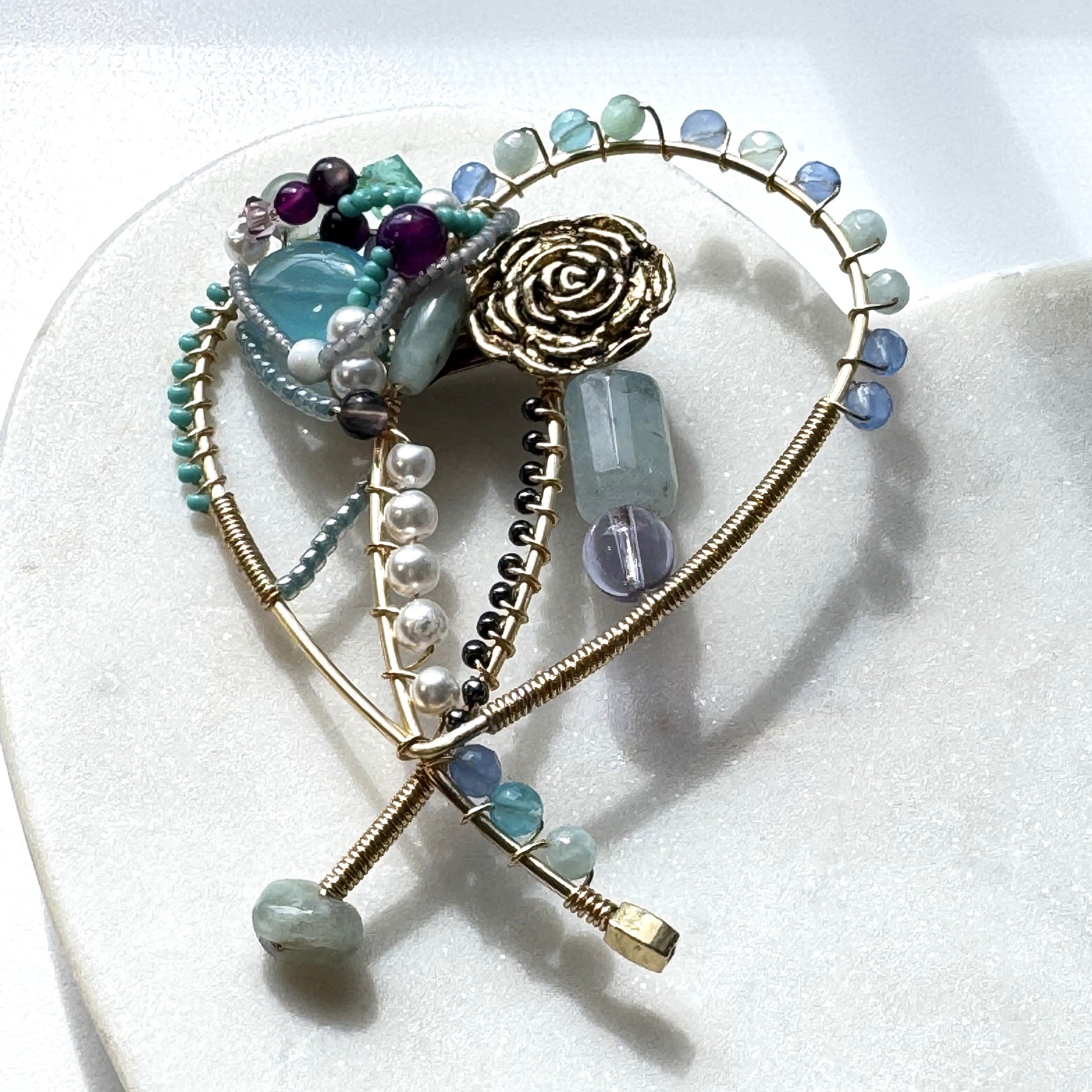 Heart-shaped brooch with gemstones and gold accents on a white background