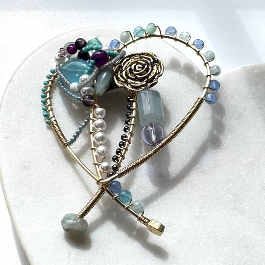 Heart-shaped brooch with gemstones and gold accents on a white background