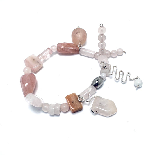 A handcrafted rose quartz bracelet featuring whimsical stone and sea glass charms, perfect for stacking or wearing alone. Rose quartz, known as the "Love Stone," is believed to open the heart to love and healing. Handmade in Canada.