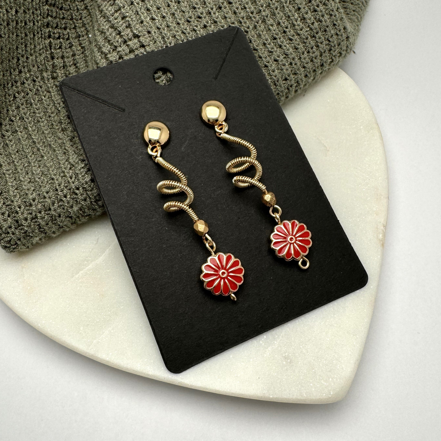 A pair of handcrafted spiral dangle earrings featuring a bold red metal flower accent. These unique earrings add a vibrant and artistic touch to any outfit. Handmade with care by Lacey & Bohème in Canada.