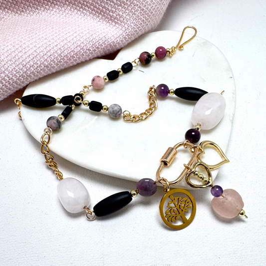 A harmonious blend of organic beauty and contemporary design, this necklace features rose quartz, amethyst, and agate beads intertwined with delicate chain elements. A stylish carabiner serves as the focal point, adorned with three symbolic charms: a Tree of Life, a heart, and pink sea glass with a gold heart. Thoughtfully handcrafted for a meaningful and versatile statement piece.