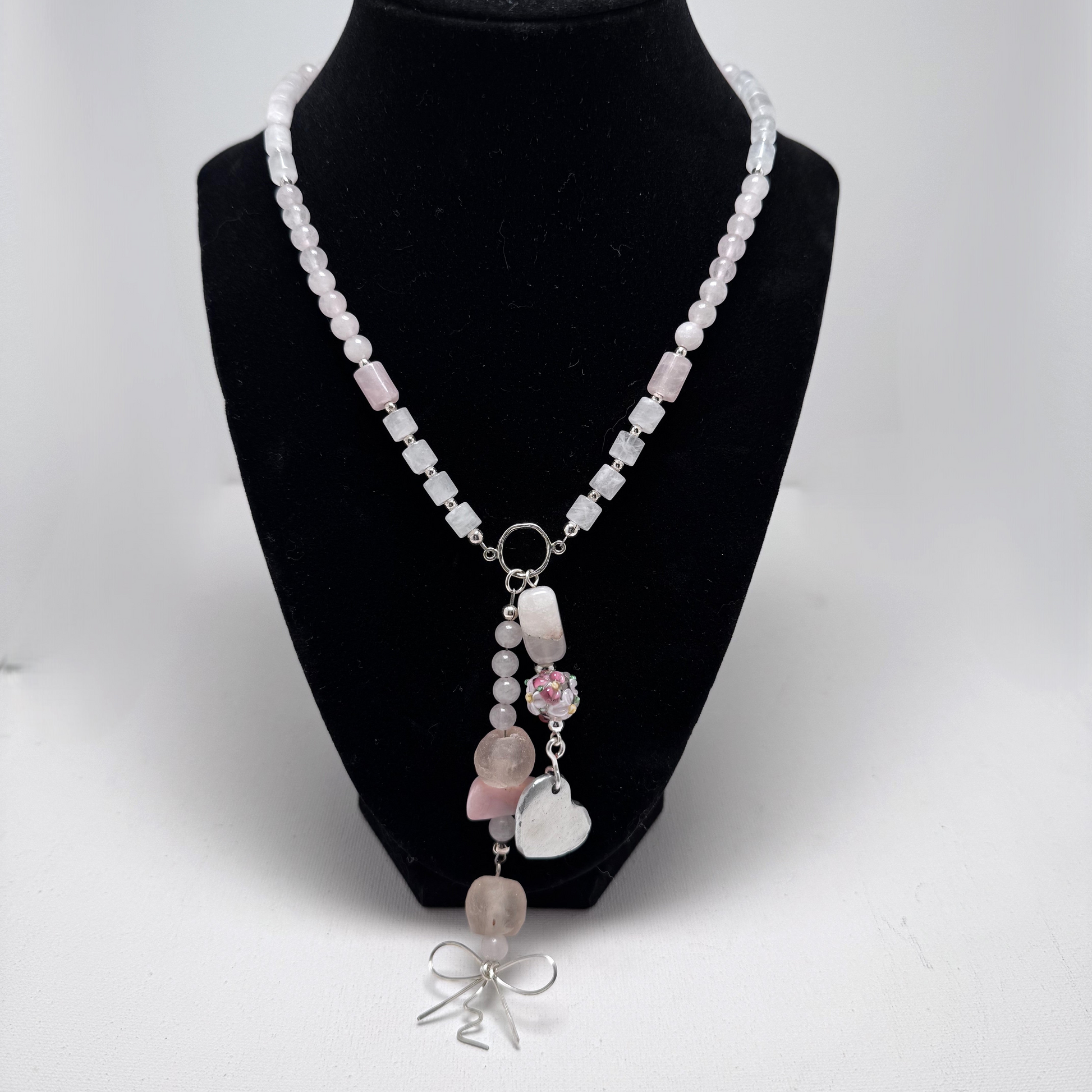 The Blush Bloom Y Necklace is a delicate, handcrafted piece featuring rose quartz, pink opal, sea glass, a floral lamp work bead, and a recycled aluminum heart. Designed with two Y-shaped pendants for a layered look, this 17.5-inch necklace embodies romance and sustainable elegance. Handmade in Canada.